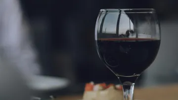Red wine in a glass is on a table with snacks.