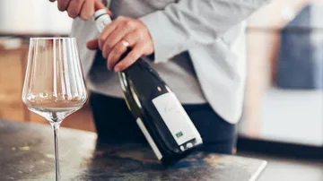 Eine Person öffnet eine Champagnerflasche neben einem Glas.