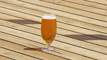 Ein Glas Bier steht auf einem Holztisch im Freien.