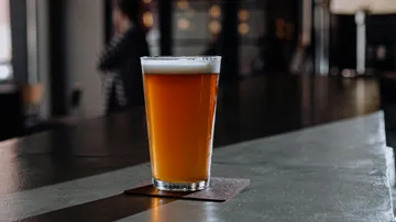 A glass of beer is on a table in a bar.