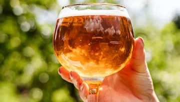A glass of brown drink is held by one hand.