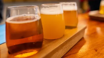 There are three glasses of beer on a wooden board.