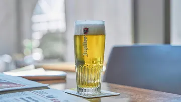 A glass of beer is on a table in a café.