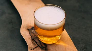 A glass of beer is on a wooden board.