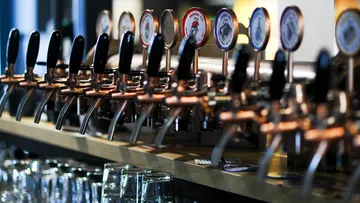 Taps fill glasses with beer in a bar setting.
