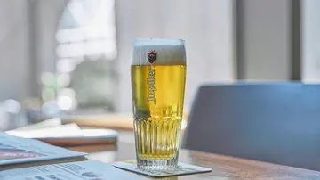 A glass of beer is on a table in a café.