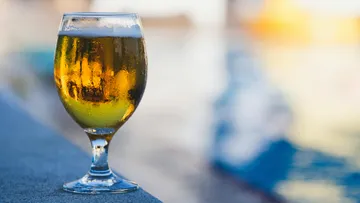 A glass of beer is on a poolside table.