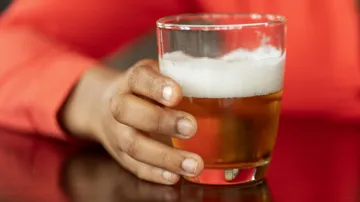 One hand holds a glass of beer on a table.