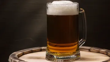 A filled beer glass stands on a wooden barrel.