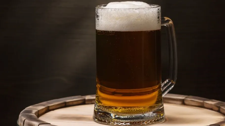 A filled beer glass stands on a wooden barrel.