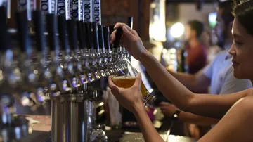 Frau zapft Bier an einer Bar in einer geselligen Umgebung.