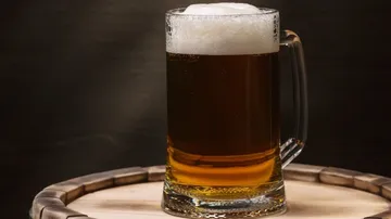 Ein Glaskrug mit Bier steht auf einem Holzfass.