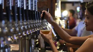 Frau zapft Bier an einer Theke in einer Bar.