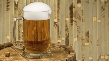 Krug Bier steht auf einem Holzfass vor Hintergrund.