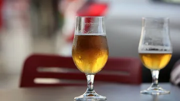 There are two glasses of beer on an outdoor table.