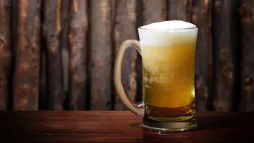 A beer mug is placed on a table in front of wooden panels.