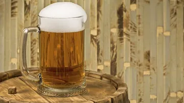 A beer mug stands on a wooden table with a background.