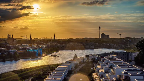 Stadtansicht mit Sonnenuntergang, Wasser und modernen Gebäuden.
