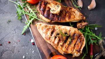 Grilled chicken breast on wooden board with side dishes.