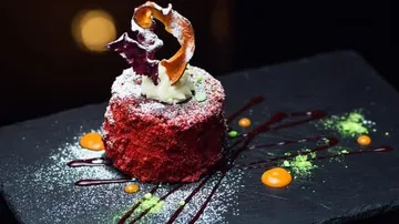 Red cake decorated with cream and fruit sauce on plate.