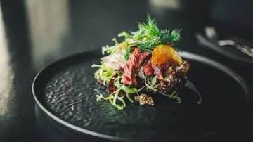 A salad dish is served on a black plate.