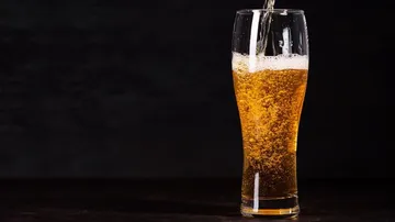 Ein Glas Bier wird gefüllt, vor dunklem Hintergrund.
