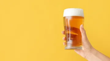 Ein Glas Bier wird von einer Hand gehalten, gelber Hintergrund.