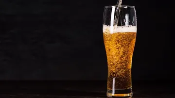 Ein Glas Bier wird eingeschenkt, vor dunklem Hintergrund.