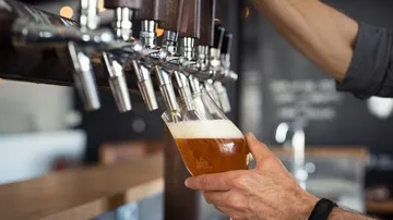A glass of beer is filled at a tap.