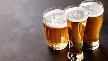 There are three glasses of beer on a dark table.