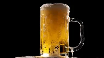 A beer mug foams and stands against a black background.