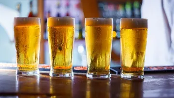 Four glasses of beer are on a table in a bar.