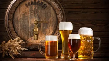 Biergläser stehen neben einem Fass in Holzumgebung.