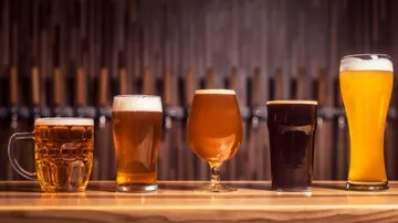 Fünf verschiedene Biergläser stehen auf einer Holzoberfläche.