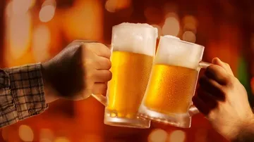 Zwei Bierkrüge stoßen an, Hintergrund mit warmem Licht.