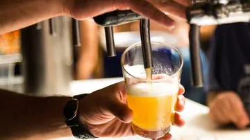 Ein Bier wird in ein Glas gezapft, in einer Bar.