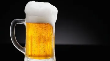 A beer mug is frothing against a dark background.