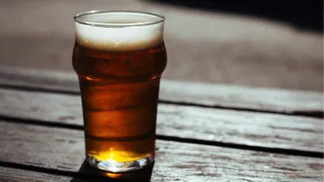Ein Glas Bier steht auf einem Holztisch in der Sonne.