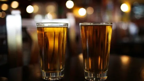 Two glasses of beer are on a table in the background.