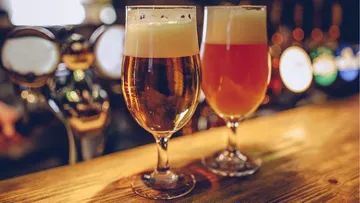 Zwei Gläser Bier stehen auf einer Holzbar.