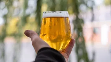 Ein Glas Bier wird in einer Hand gehalten.