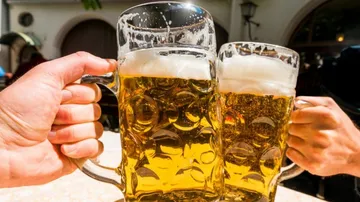 Zwei Bierkrüge stoßen an, im Freien bei sonnigem Wetter.