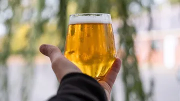 Ein Glas Bier wird von einer Hand gehalten, draußen.