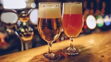 There are two glasses of beer on a wooden bar.
