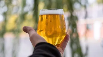 A glass of beer is held in one hand, the background is blurred.