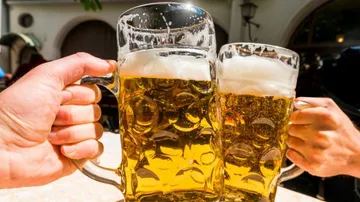 Two beer mugs are thrown together, outdoors, sunny.