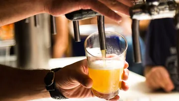 A glass of beer is filled at a tap.