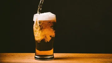 Ein Glas Bier wird gefüllt, auf einem Holztisch stehend.