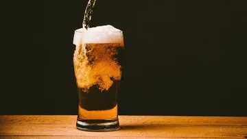 A glass of beer is poured onto a wooden table.