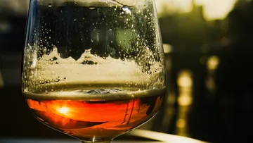 Ein Glas mit Bier reflektiert Sonnenlicht im Hintergrund.